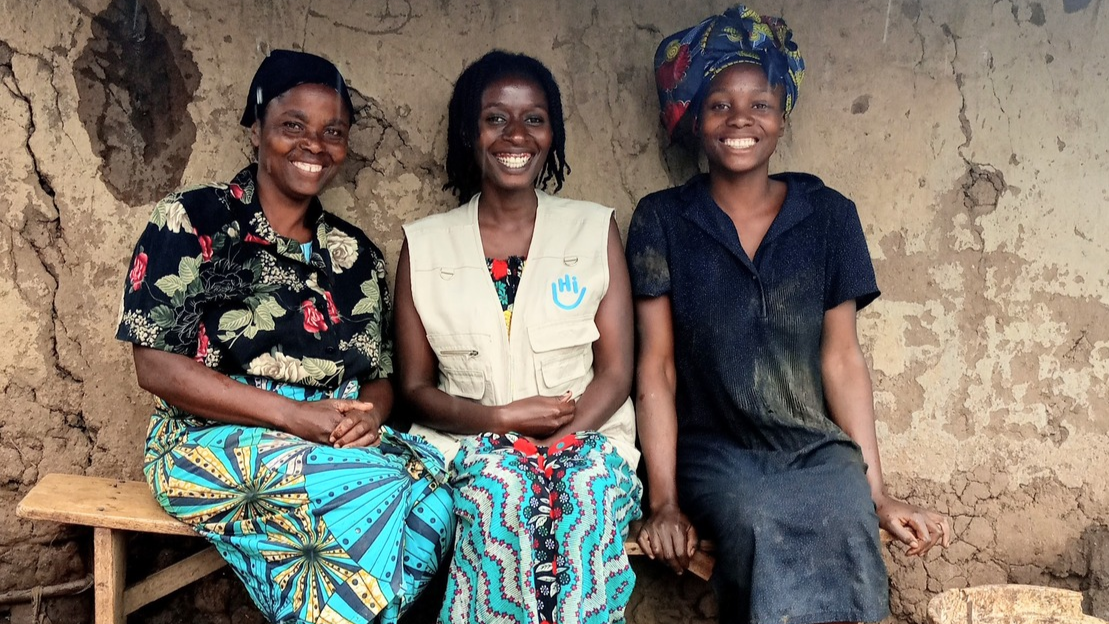 Béatrice, een psychosociaal werker van Handicap International, en Rose zitten op een bankje voor hun huis. De drie vrouwen glimlachen.