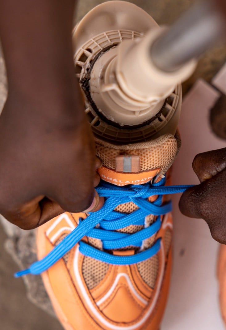 Des mains d'enfants nouent des lacets bleus sur des chaussures oranges avec une prothèse.