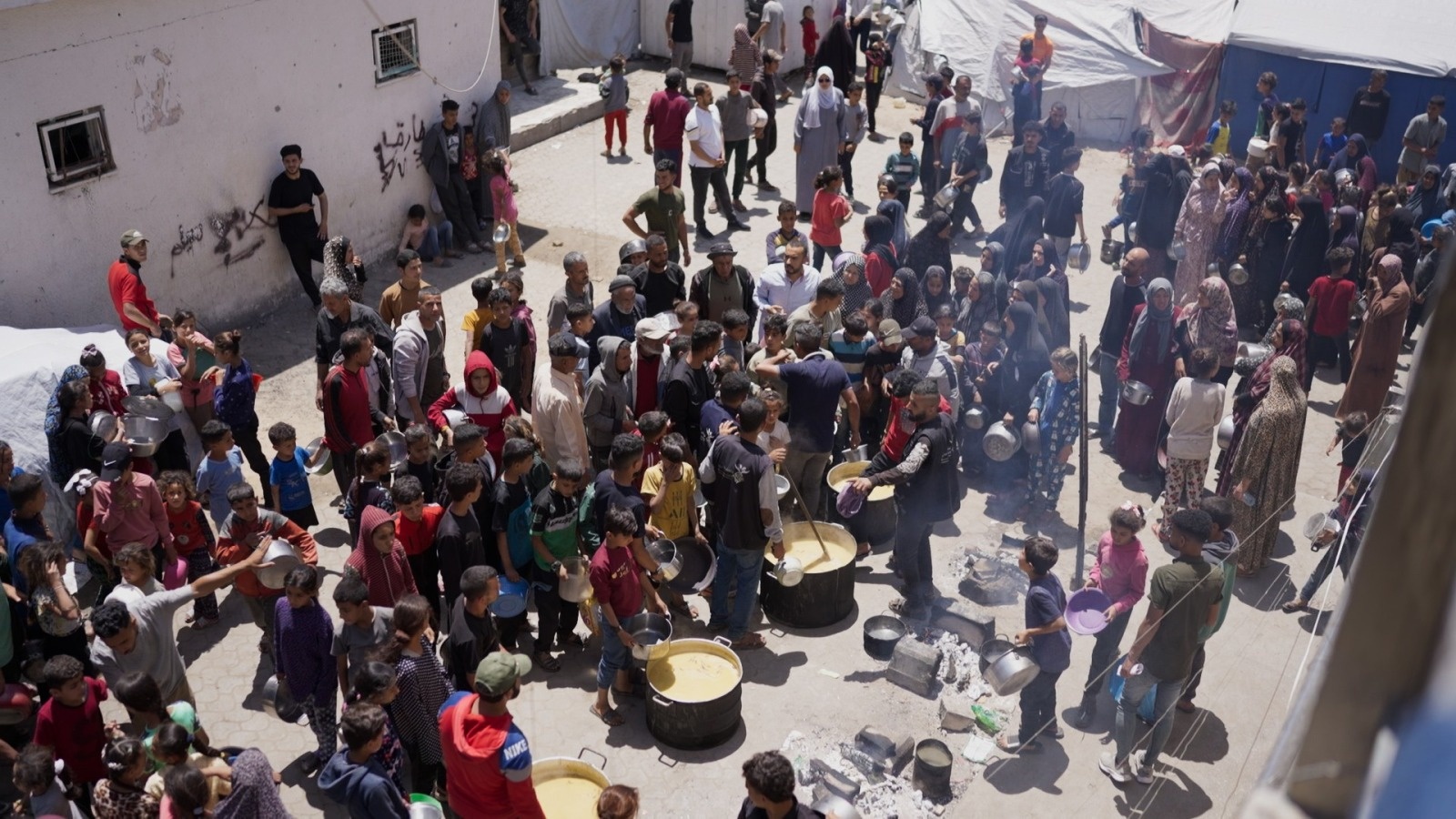 Un grand groupe de personnes devant de grandes marmites attendent de recevoir de la nourriture.