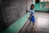Longini, jeune garçon rwandais de 9 ans, en classe debout sur ses deux prothèses, écrit au tableau  