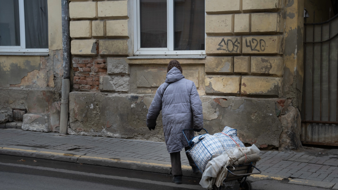 Une personne en manteau tire une charrette remplie de sacs dans une rue abîmée en hiver.