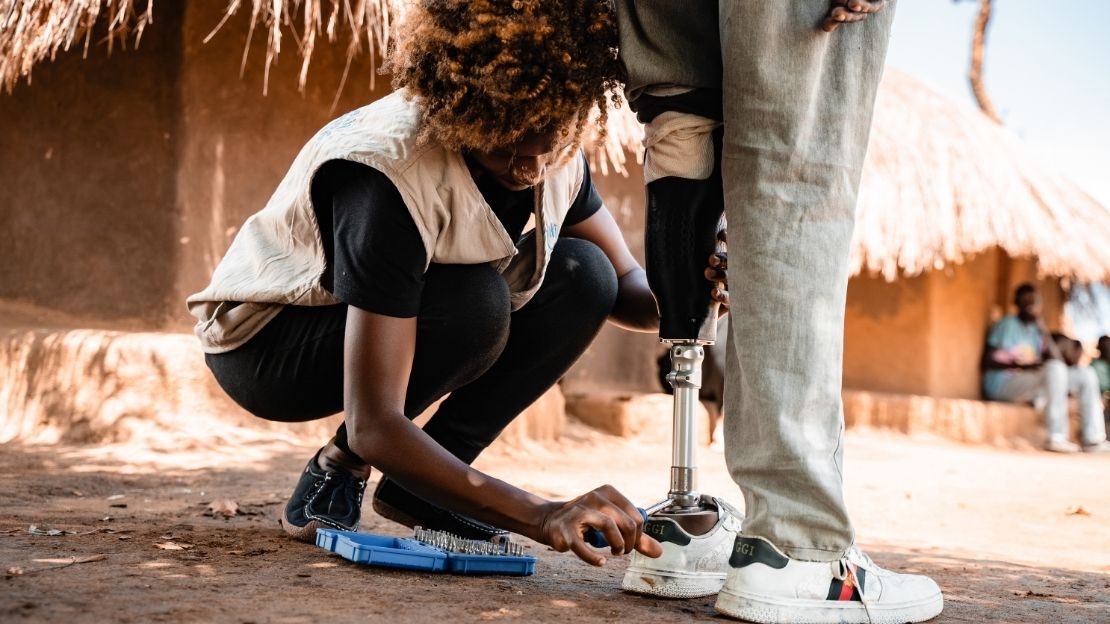 Une femme utilise un tournevis pour travailler sur la prothèse de jambe d'une personne debout.