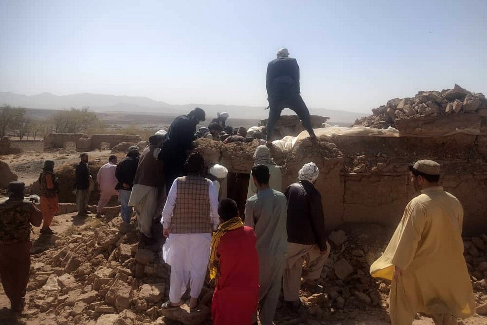 Un groupe de personnes se rassemble sur une colline rocheuse jonchée de gravats, sous un ciel dégagé. Elles semblent préoccupées et concentrées, engagées dans un effort coordonné.