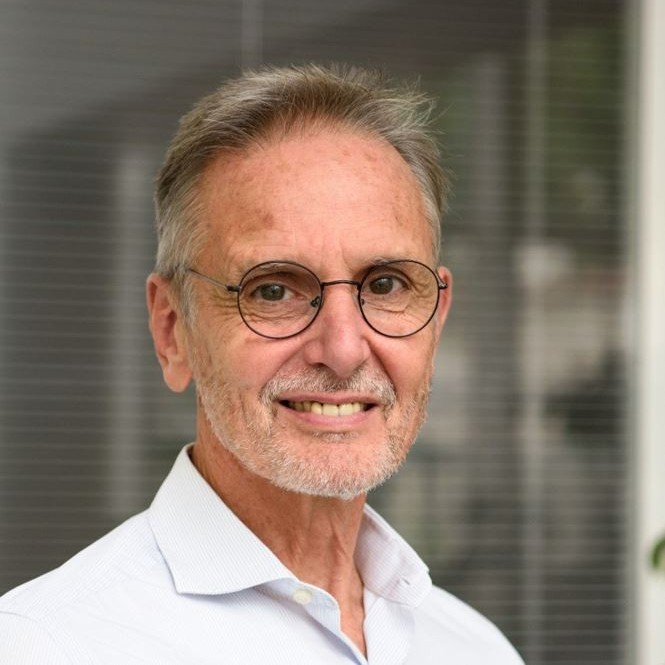 Un homme souriant portant des lunettes et une chemise blanche.