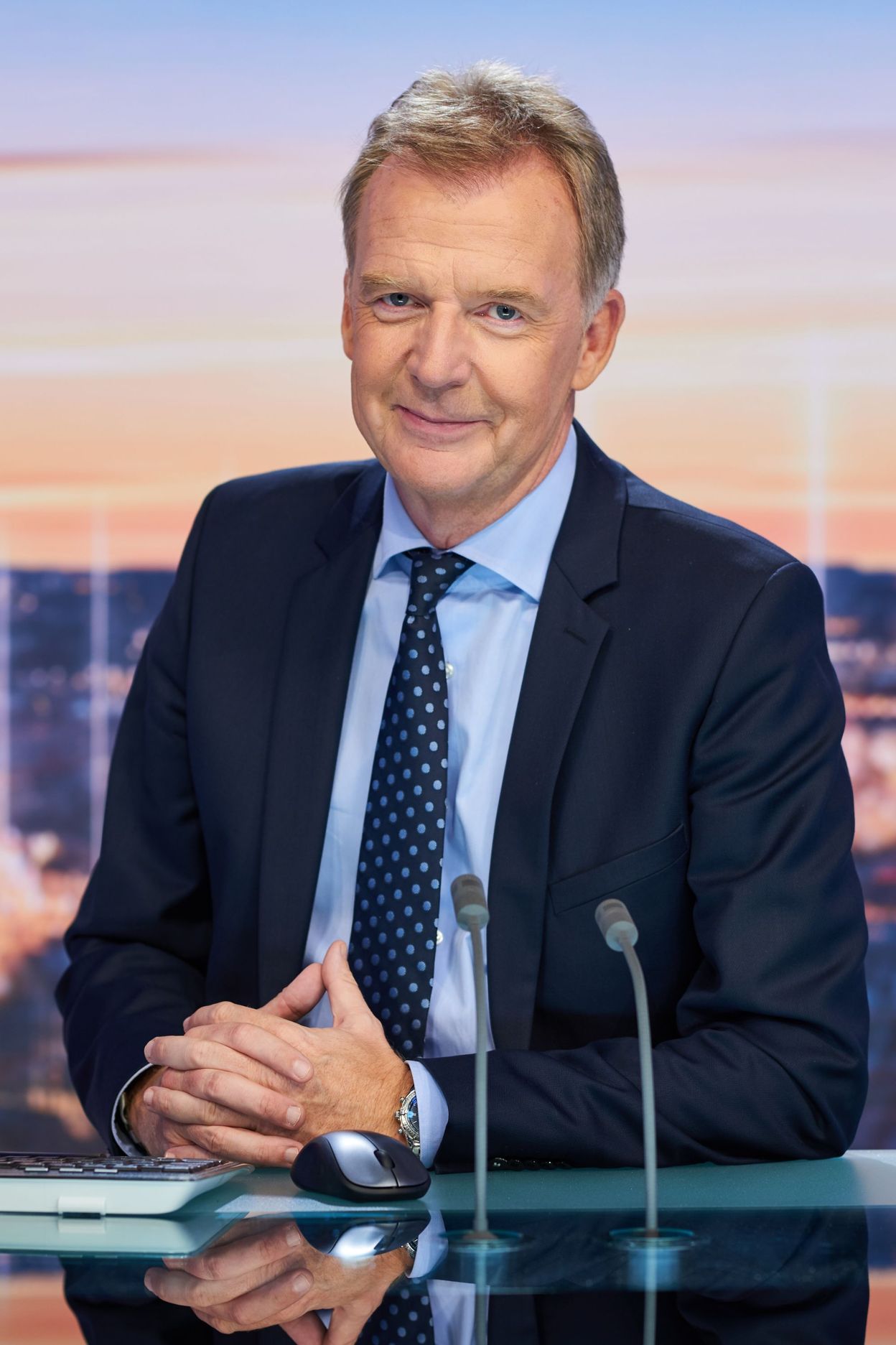 Un homme en costume et cravate, assis à un bureau, avec un air professionnel.