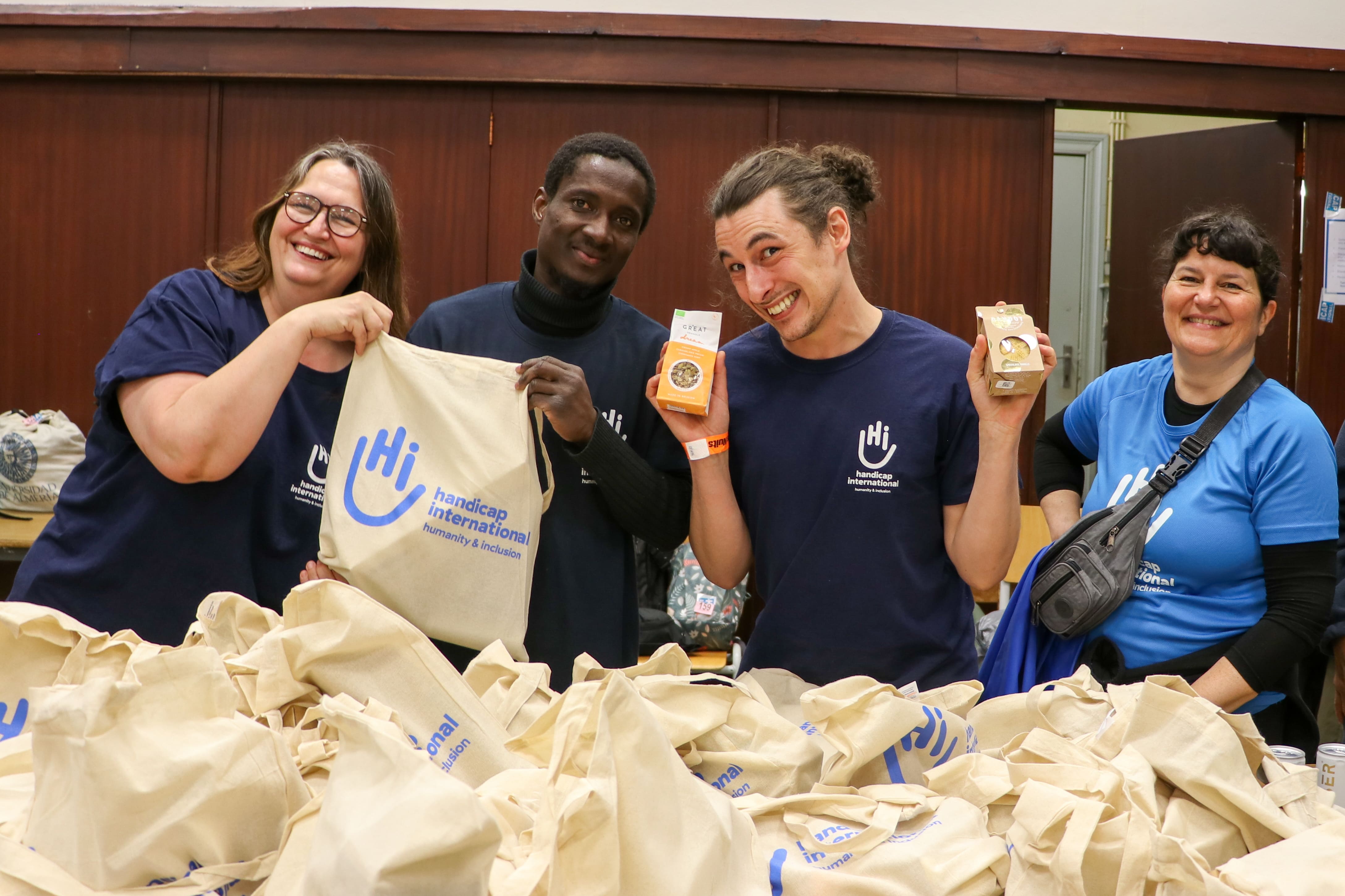 Quatre bénévoles de Handicap International souriants préparent des sacs de ravitaillement pour les participants des 20 km de Bruxelles.