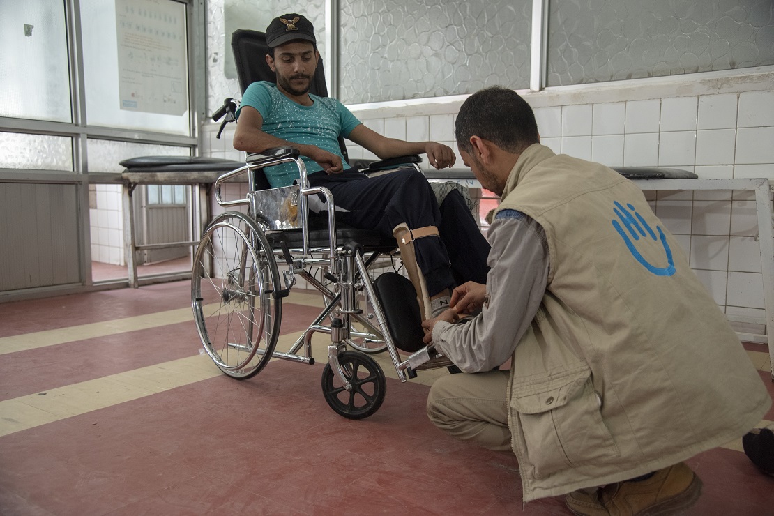 Un homme jeune assis dans une chaise roulante. Un spécialiste de Handicap International examine son orthèse.