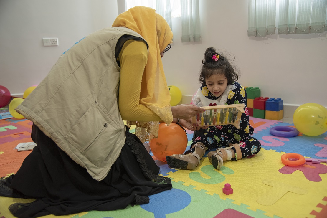 Een expert toont een blad aan een klein meisje dat op een speelmat zit.
