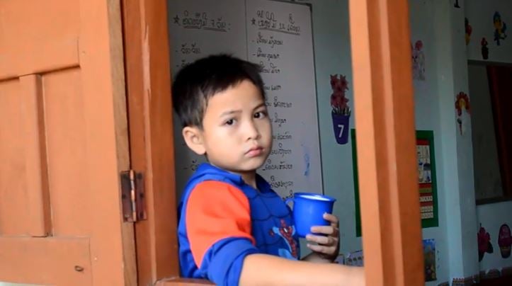 Un petit garçon posté à l'entrée de sa salle de classe / A young boy standing at the door of his classroom 