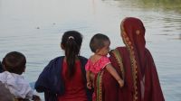 Een vrouw en enkele kinderen kijken naar een ondergelopen dorp