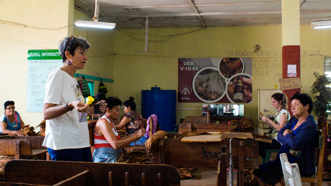 Dans une salle, une femme tient à la main une coupe menstruelle et en explique le fonctionnement. D'autres femmes sont assises sur des bancs autour et l'écoutent.
