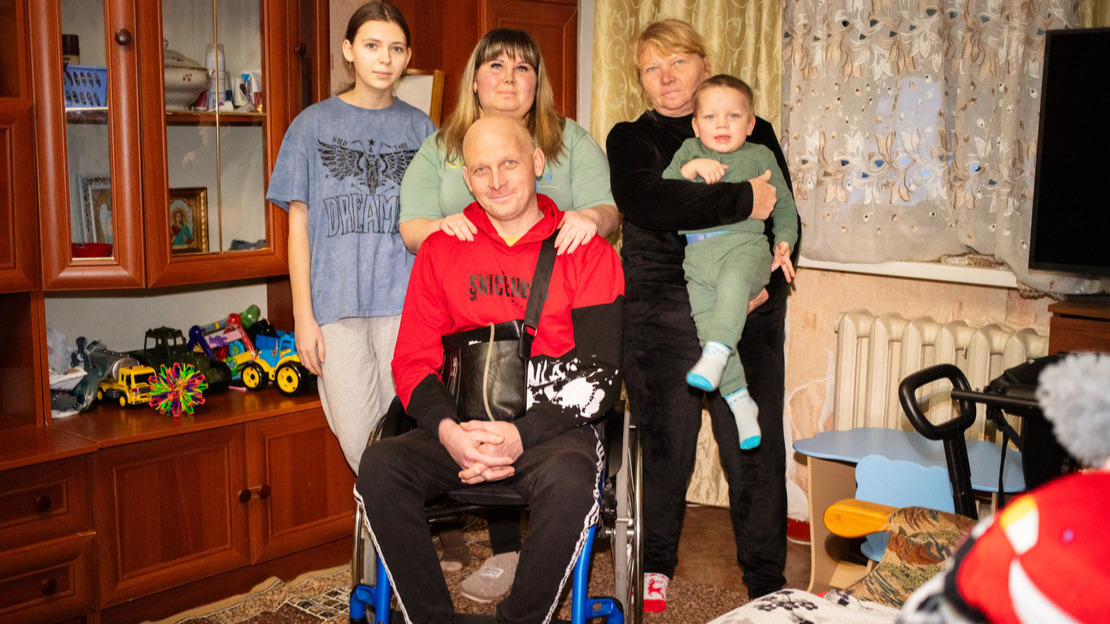Un homme est assis dans un fauteuil roulant dans un appartement avec autour de lui sa famille.