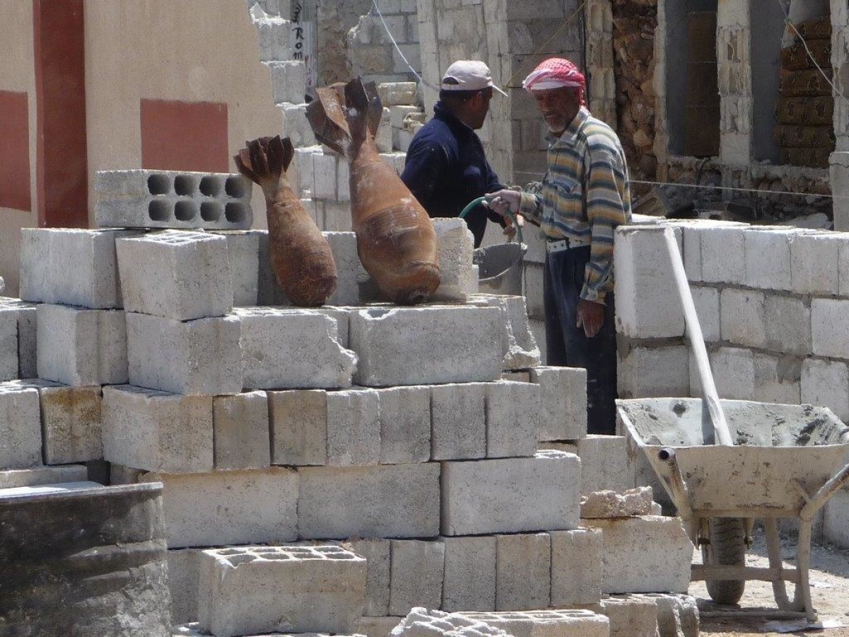 deux hommes âgés debout entre des matérieaux de construction où sont posés deux engins de guerre non explosés