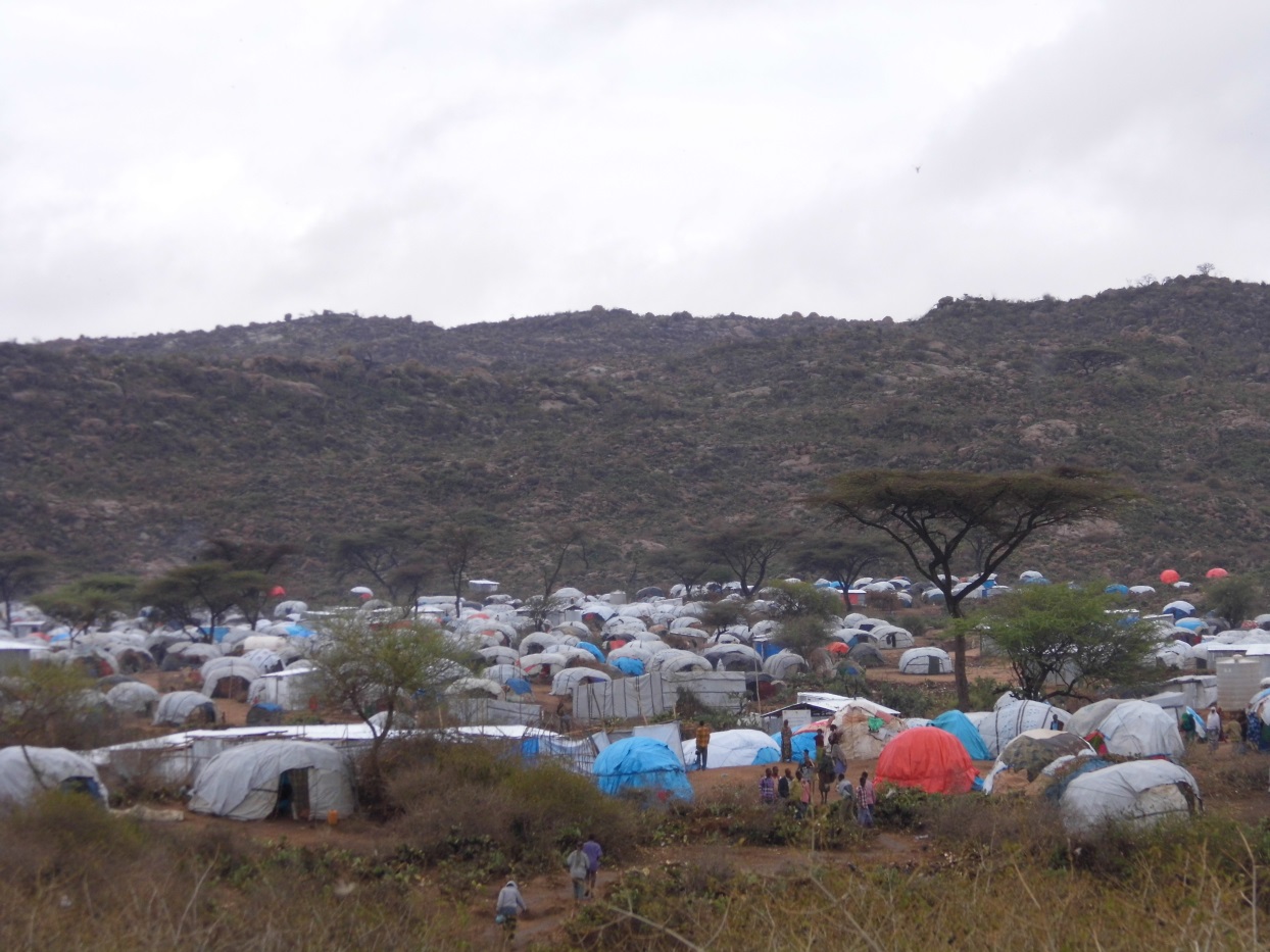 Un camp de tentes avec des dizaines de tentes. Des personnes marchent sur des chemine entre les abris