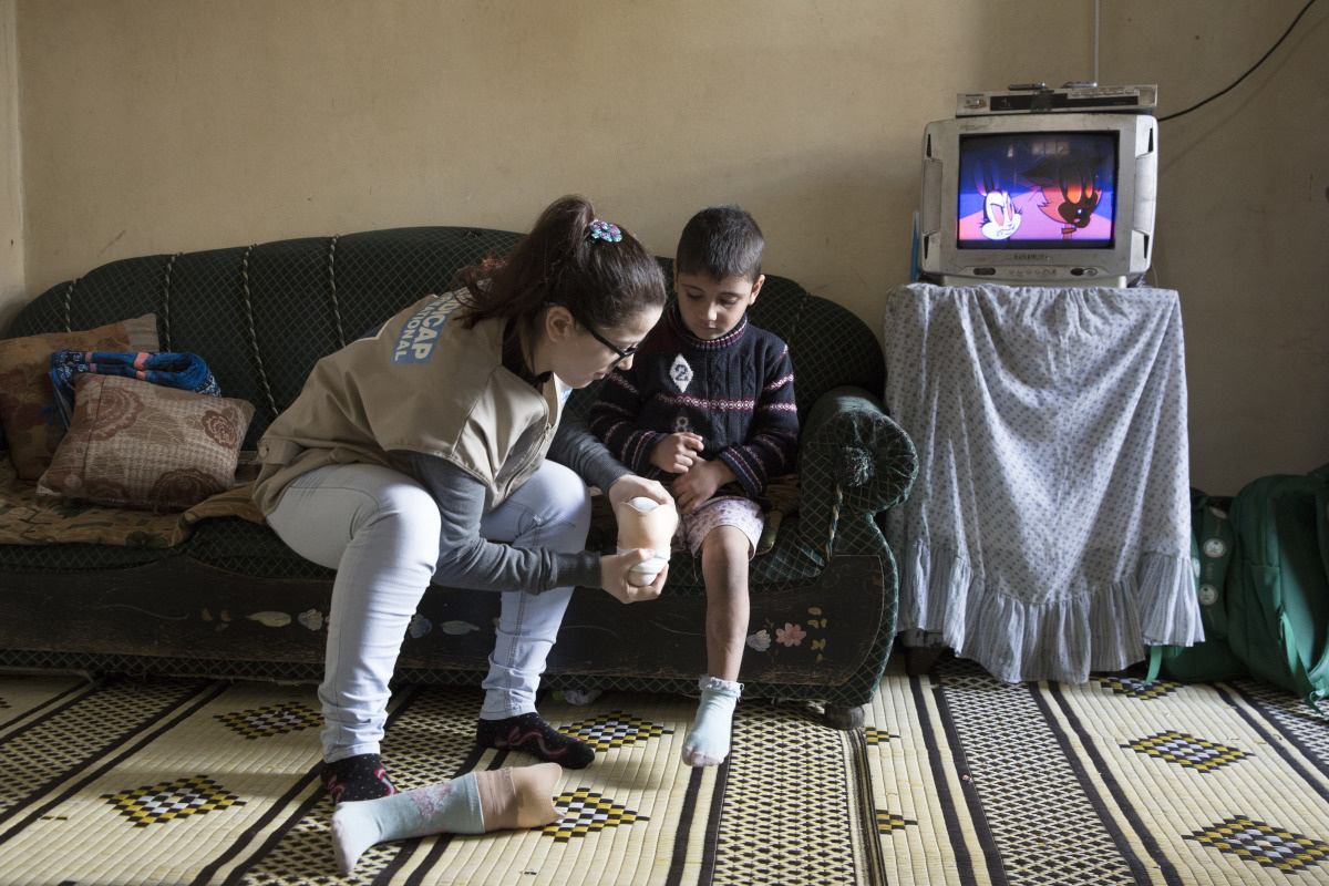 Un jeune garçon amuté de la jambe droite, soigné par un kinésithérapeute de Handicap International in een woonkamer