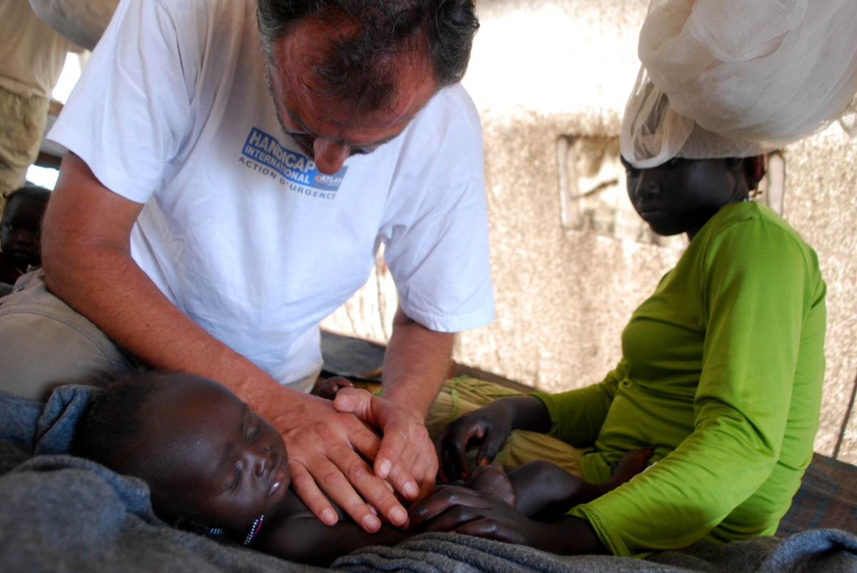 Un kinésithérapeute de Handicap International pousse avec ses mains sur la cage thoracique d'un bébé souffrant de malnutrition, sous le ragard d'une jeune femme