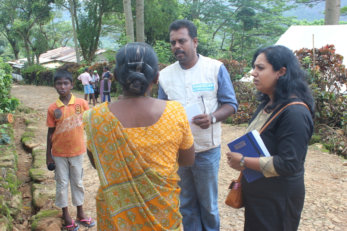 Un membre de l'équipe d'aide de Handicap International parle avec une Sri Lankaise en sari jaune, vue de dos.